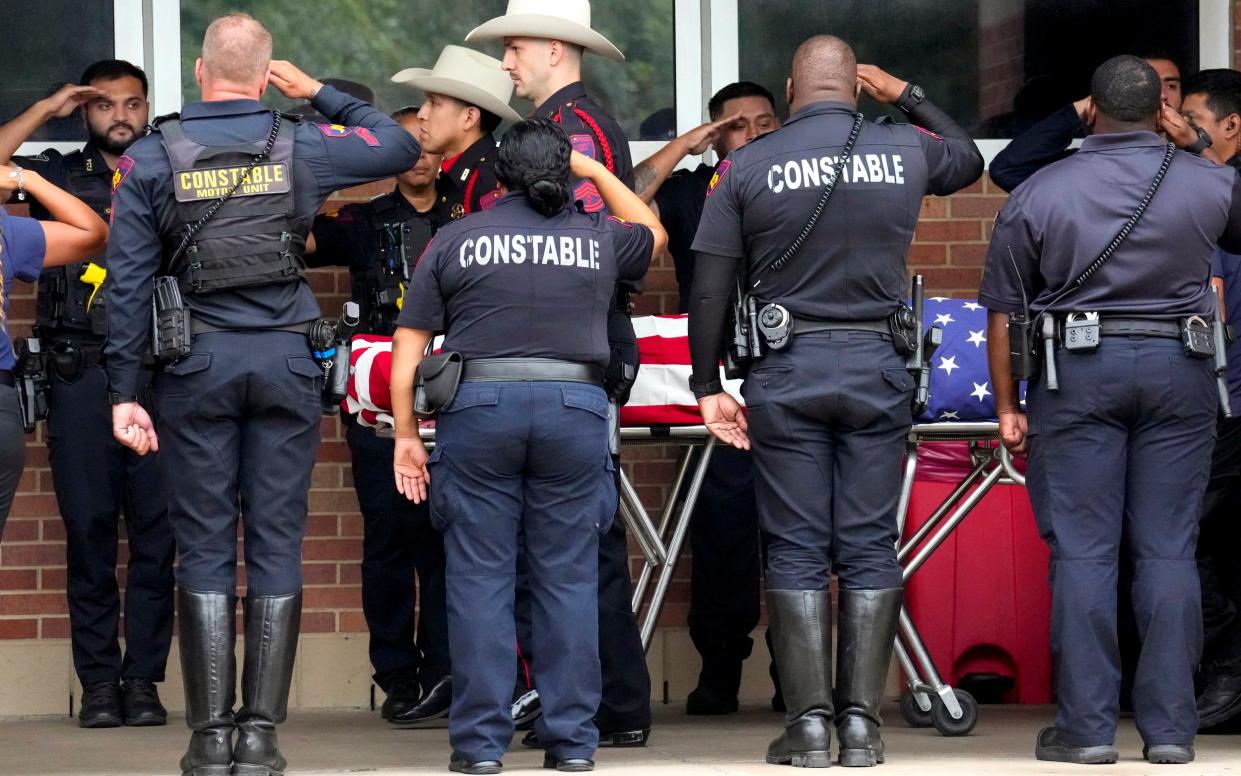 Police officers salute the flag-draped body of Deputy Constable Husseini