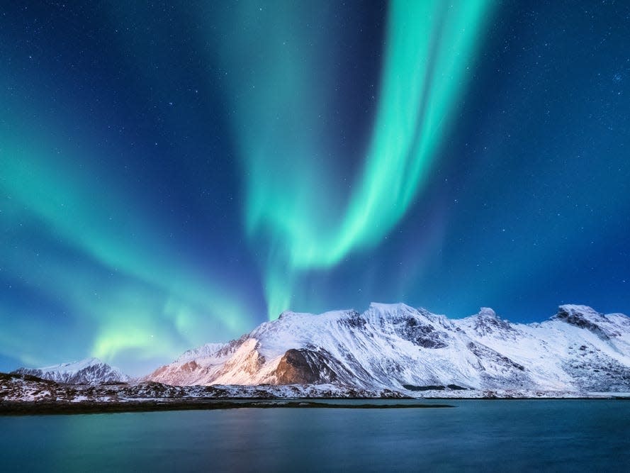 The northern lights over snowy mountains by the water.