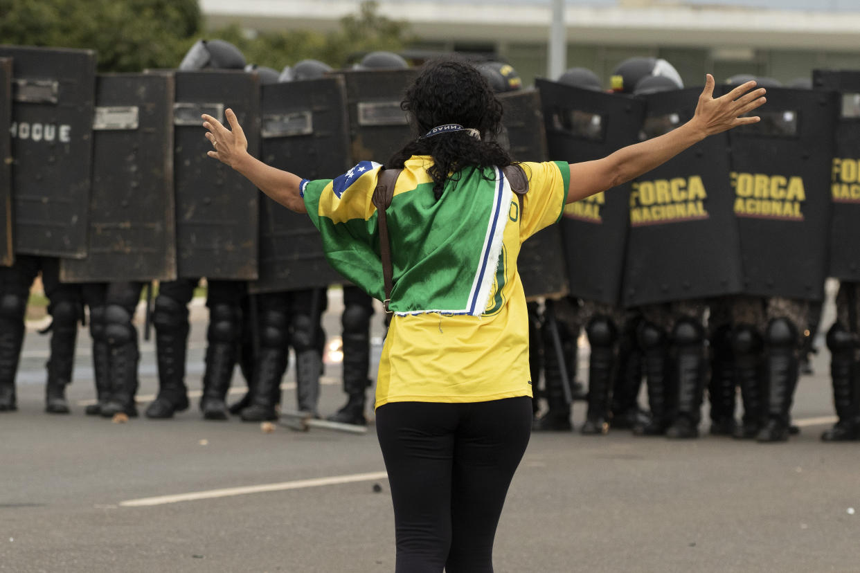 A supporter of former President Jair Bolsonaro outstretches her arms in front of a phalanx of security forces at the National Congress