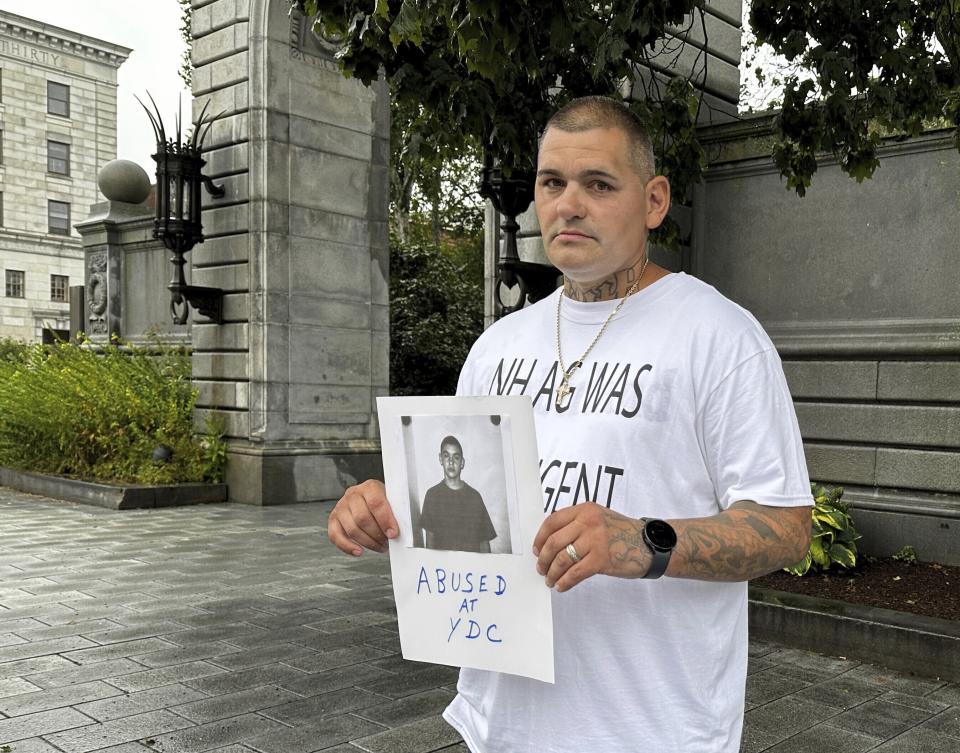 Michael Gilpatrick holds a copy of his intake photo from New Hampshire's youth detention center as he and other former residents of the Youth Development Center, now called the Sununu Youth Services Center, hold a rally outside the Statehouse in Concord, Friday, Aug. 25, 2023, to press for a federal investigation into their claims of physical and sexual abuse. (AP Photo/Holly Ramer)