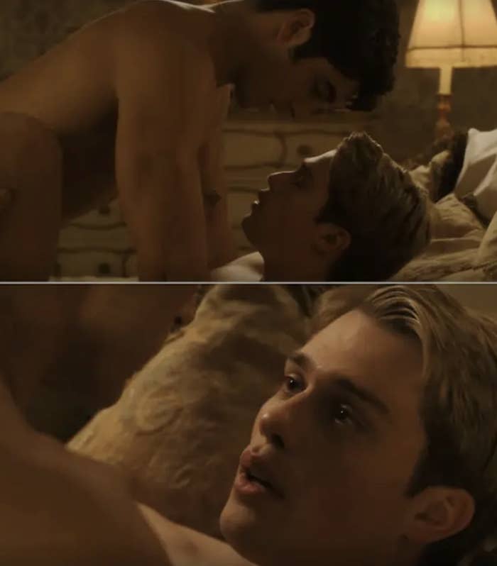 Two shirtless men, one lying on a bed and the other on top, engage in an intimate moment