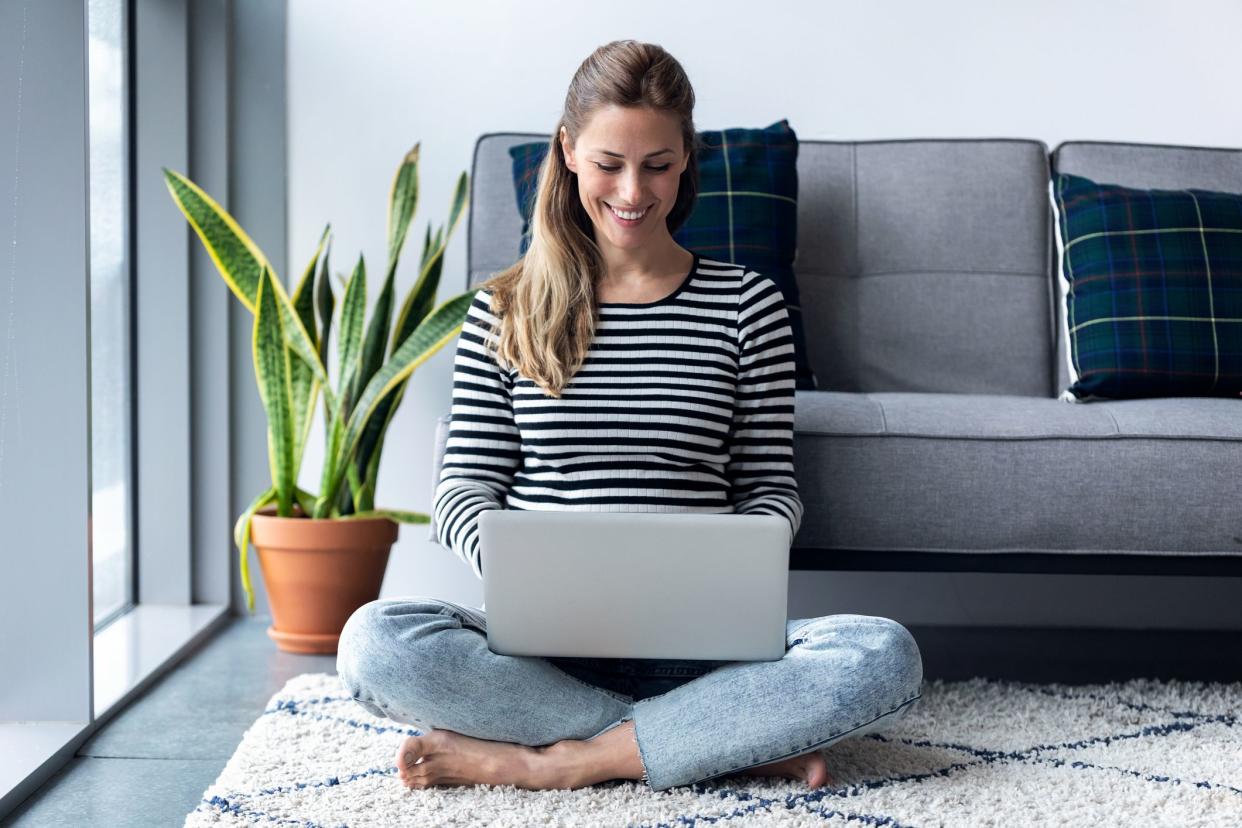 Shot of pretty young woman using her laptop while sitting on the floor at home.