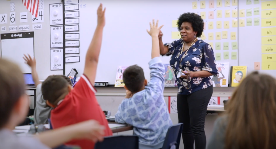 Students raising hands in front of teacher