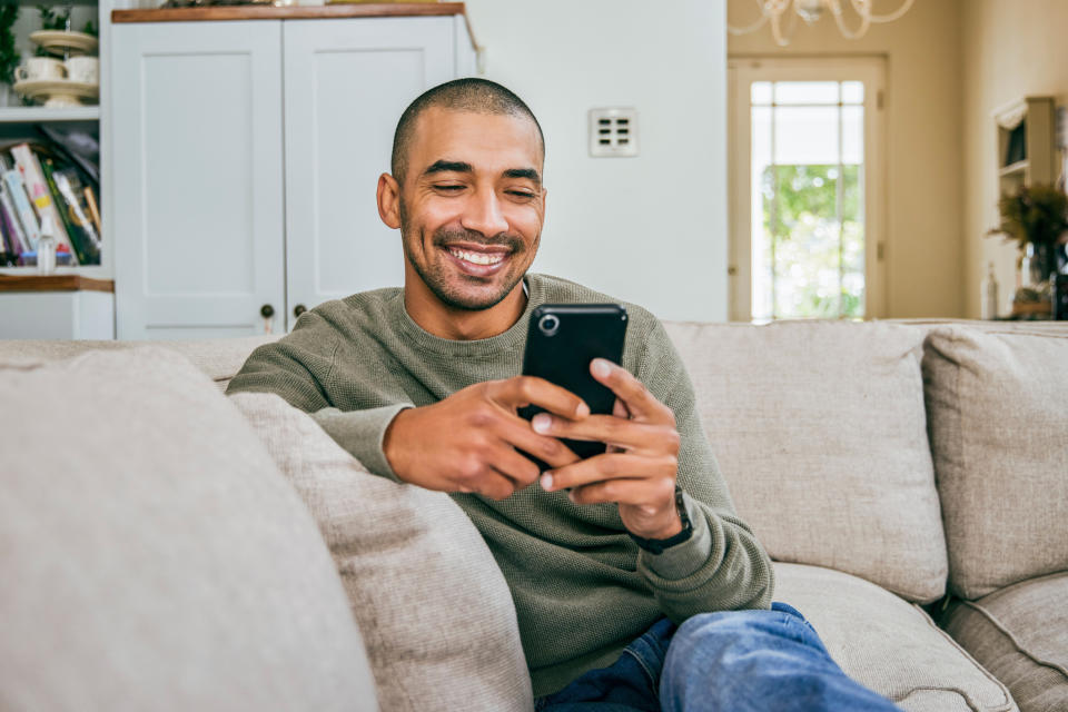 Smiling man in a casual sweater and jeans sitting on a sofa, looking at his phone