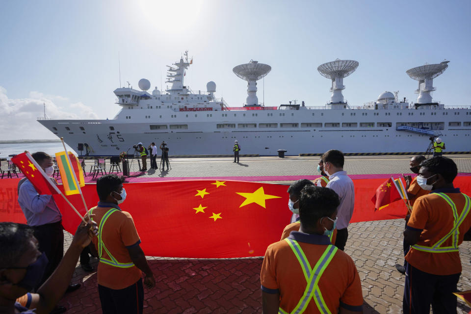 FILE - Sri Lankan port workers hold a Chinese national flag to welcome Chinese research ship Yuan Wang 5, bristling with surveillance equipment, as it arrives in Hambantota International Port in Hambantota, Sri Lanka, Tuesday, Aug. 16, 2022. In 2022, the country went into default, unable to make even interest payments on loans financing the construction of ports, roads and railways. (AP Photo/Eranga Jayawardena, File)