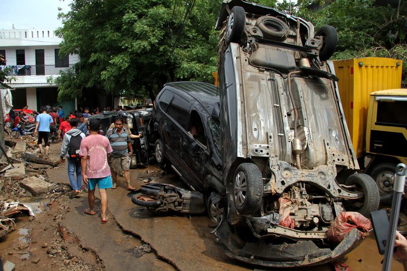 People pass vehicles damaged by floods after heavy rains in Bekasi, near Jakarta