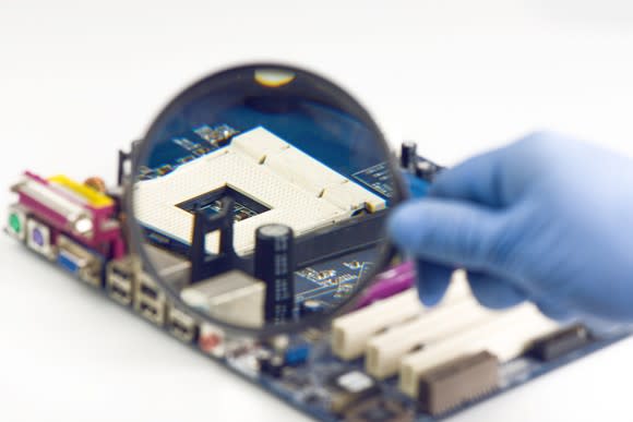 Gloved hand holding up a magnifying glass in front of an empty processor socket.