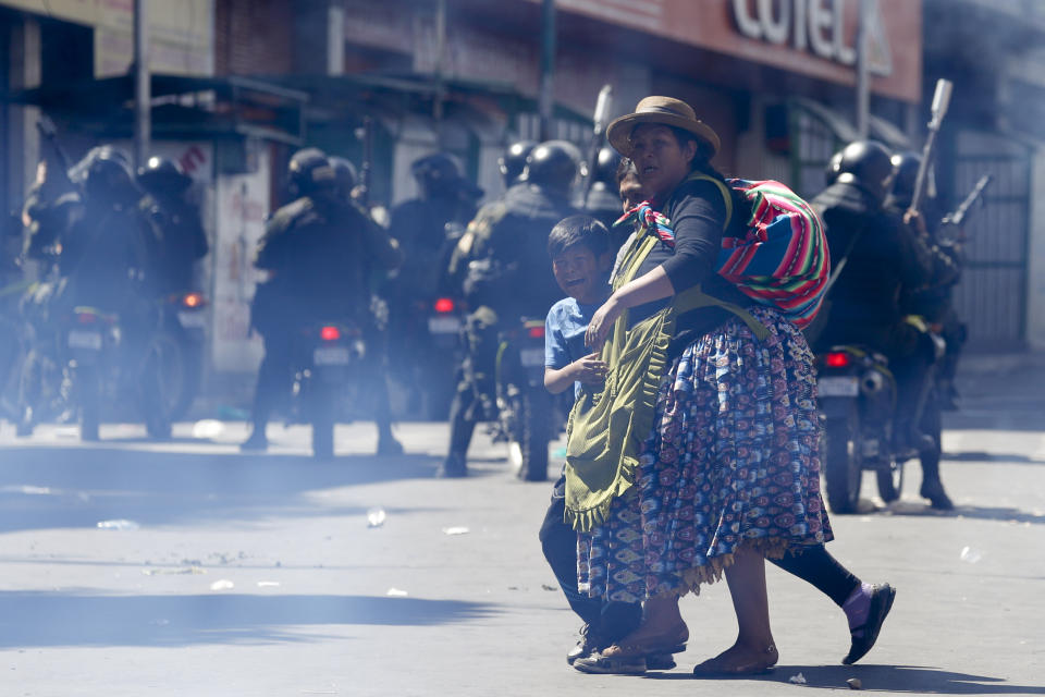 A woman crosses a street with a child crying aloud during clashes between supporters of former President Evo Morales and security forces, in La Paz, Bolivia, Thursday, Nov. 21, 2019. In an attempt to curb the social upheaval in Bolivia, interim President Jeanine Anez sent a bill to Congress to call for new elections amid an escalation of violence that has left 30 people dead. (AP Photo/Natacha Pisarenko)