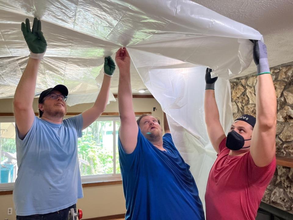 Left to right: Matthew Wardell, Chad Taylor and Jason Lugauskas put protective plastic covering in place at Taylor's home on July 1.