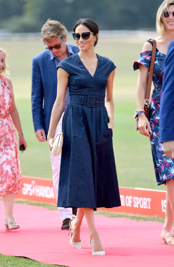 Meghan Markle wears a Carolina Herrera belted denim midi dress, Tom Ford sunglasses, J.Crew clutch, and Aquazzura heels at Royal County of Berkshire Polo Club on July 26, 2018. (