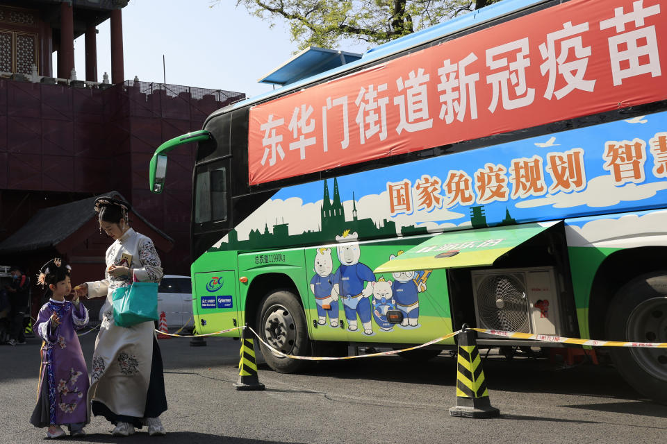 A woman and child wearing period costumes pass by a bus providing COVID-19 vaccination outside the Forbidden City in Beijing on April 14, 2021. If China is to meet its tentative goal of vaccinating 80% of its population against the coronavirus by the end of the year, tens of millions of children may have to start rolling up their sleeves. (AP Photo/Ng Han Guan)