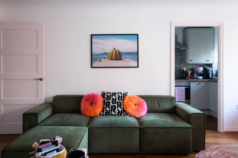 Green couch with colorful pillows anchors white living room.