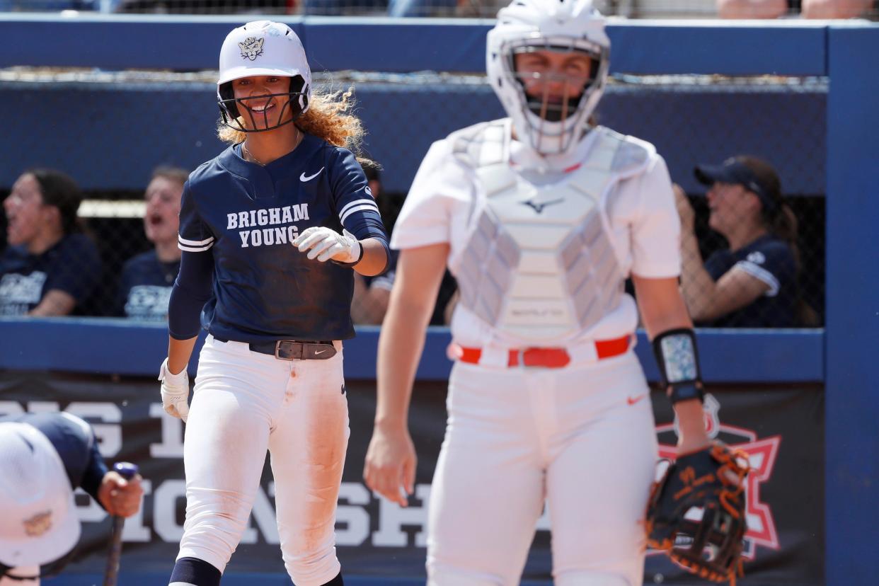 BYU's Lily Owens (13) smiles behind OSU catcher Caroline Wang (66) after scoring a run in the second inning of a 7-2 win in the Big 12 softball quarterfinals Thursday at Devon Park.
