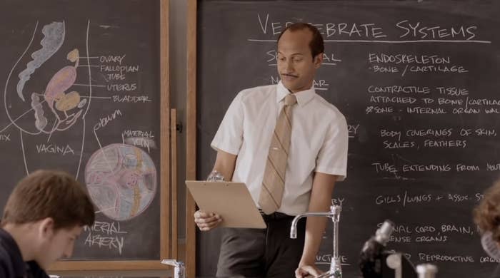 Teacher with clipboard in front of a chalkboard labeled "Vertebrate Systems" in a classroom scene