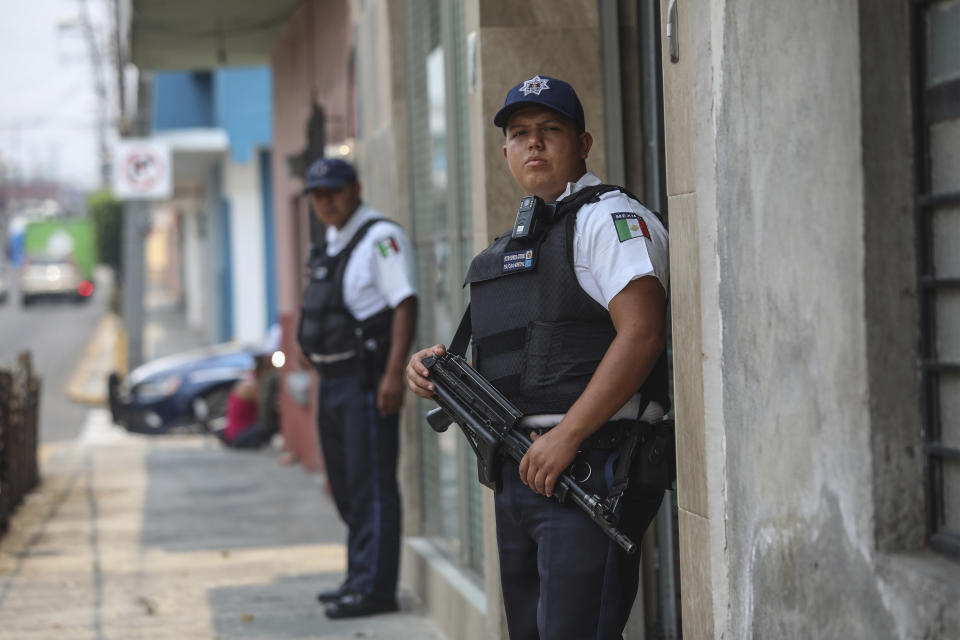 Municipal police officers stand guard on the street where the forensic office is located, where the bodies of Mixtla de Altamirano Mayor Maricela Vallejo, her husband and her driver were taken in Orizaba, Veracruz state, Mexico, Thursday, April 25, 2019. Prosecutors said the three came under fire from behind and both sides of their SUV while traveling on a highway. (AP Photo/Felix Marquez)