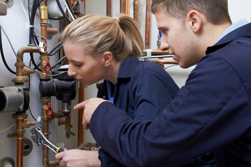 A man points at a pipe that a woman is working on with a wrench.