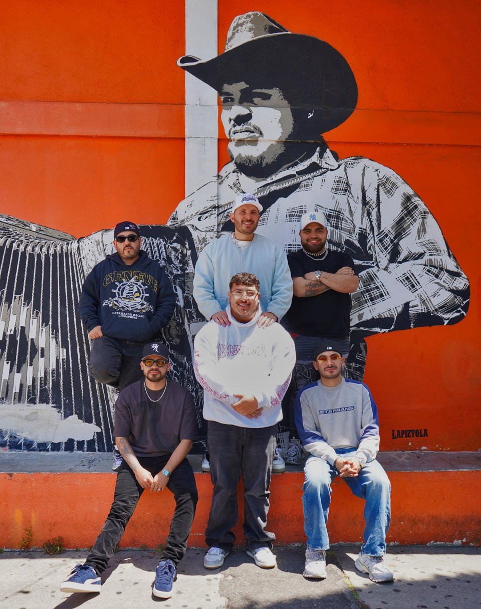 Grupo Frontera pose for a portrait against an orange mural featuring a man in a cowboy hat (Sam Kubota / TODAY)