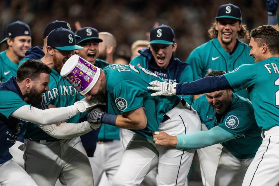 Seattle Mariners including Jesse Winker, left; Ty France, third from right; Logan Gilbert, second from right; and Adam Frazier, right celebrate a home run by Cal Raleigh in ninth inning of a baseball game against the Oakland Athletics, Friday, Sept. 30, 2022, in Seattle. The Mariners won 2-1 to clinch a spot in the playoffs.