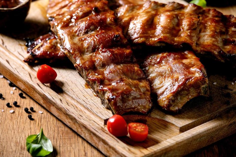 grilled pork bbq ribs served with cherry tomatoes basil and barbeque sauce on wooden cutting board on wood board close up