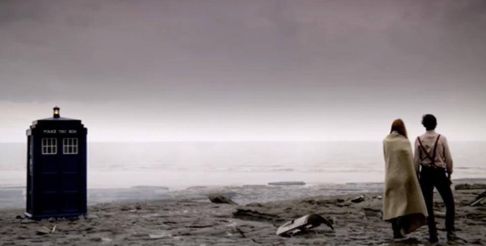 A still from "Doctor Who" of the Doctor and Amy standing on a beach next to the Tardis