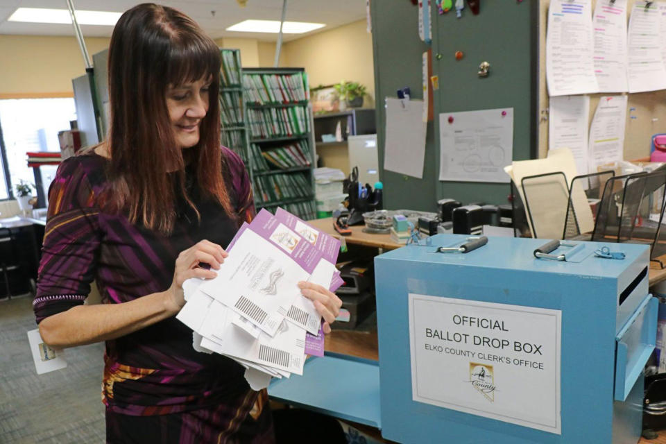 Elko County Clerk Kris Jakeman looks at a batch of mail-in ballots pulled out of an official ballot drop box for a school bond special election in her office in Elko, Nev., on Dec. 14, 2021. In Elko County, the long-time clerk decided to run for re-election last minute, after considering stepping down. Commissioners there want to do away with voting machines. (Elko Daily Free Press via AP)