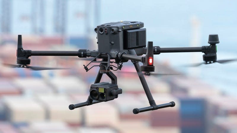 An in-flight shot of the DJI Matrice 350 RTK drone with an out-of-focus collection of shipping containers in the background.