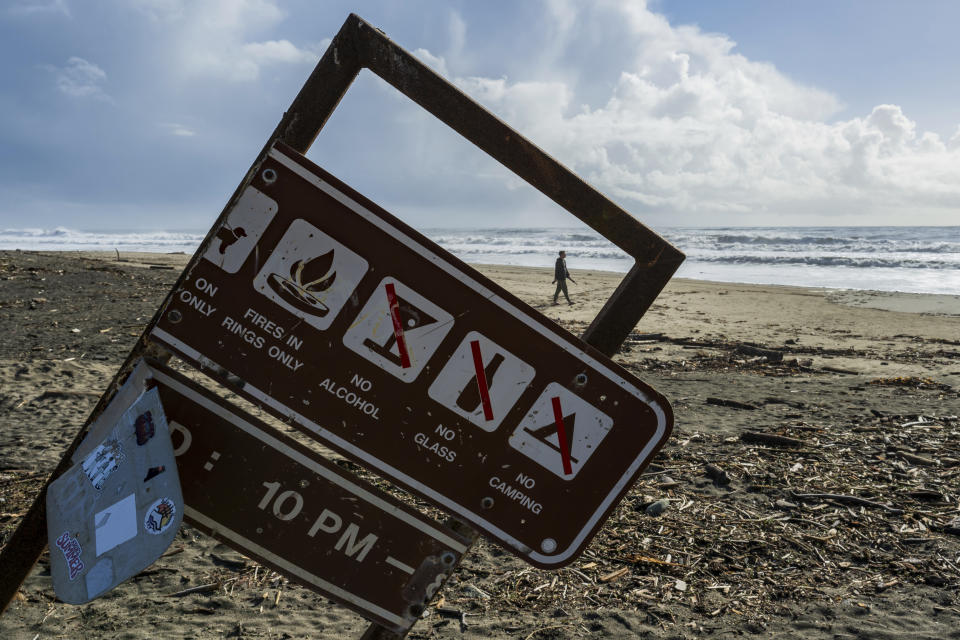 A man walks along Rio Del Mar beach near a sign damaged in recent storms Thursday, Feb. 1, 2024, in Aptos, Calif. The first of two back-to-back atmospheric rivers drenched California on Thursday, flooding roads and toppling trees while triggering statewide storm preparations and calls for people to get ready for powerful downpours, heavy snow and damaging winds.(AP Photo/Nic Coury)