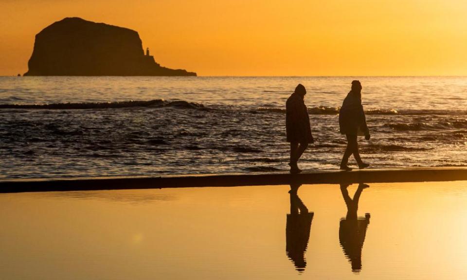 A couple walk along the beach at North Berwick, East Lothian at sunrise.