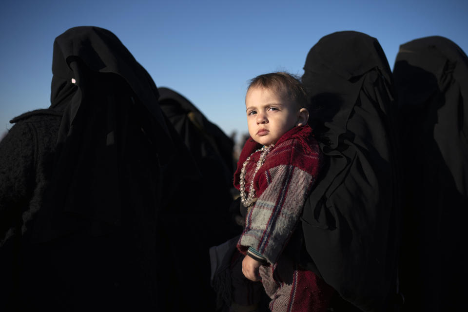 A woman holds a child as she waits to be screened by U.S.-backed Syrian Democratic Forces (SDF) after being evacuated out of the last territory held by Islamic State militants, in the desert outside Baghouz, Syria, Friday, March 1, 2019. (AP Photo/Felipe Dana)