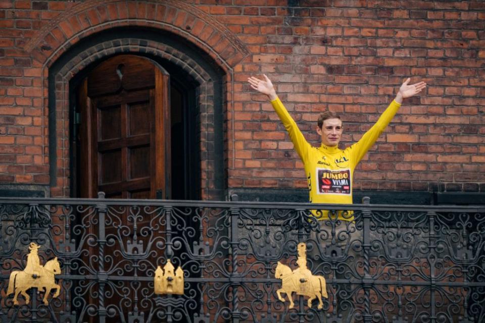 Jonas Vingegaard waves at crowds from a balcony in Copenhagen, wearing the Tour de France yellow jersey