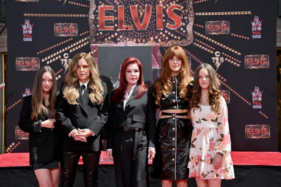 harper lockwood, lisa marie presley, priscilla presley, riley keough, and finley lockwood pose for a photo together while standing in front of an elvis movie backdrop