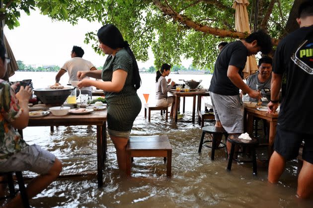 Diners stand while eating at the Chaopraya Antique Cafe as floodwaters from Thailand's Chao Phraya River surge into the restaurant in Nonthaburi province, north of Bangkok, on Oct. 7. (Photo: LILLIAN SUWANRUMPHA/AFP via Getty Images)