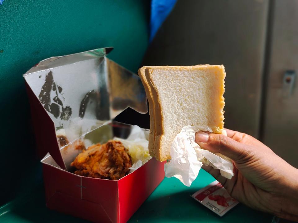 hand holding up a piece of bread in front of a box of food on a train