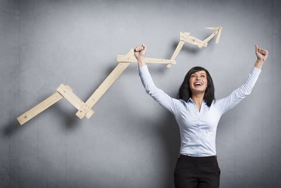 A cheering young businesswomen in front of a rising wooden chart line.