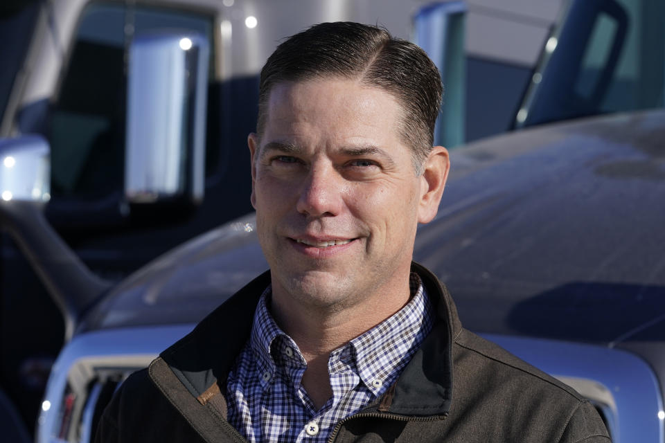 Aaron Tennant stands in front of vehicles in the lot of his trucking and shipping company, Monday, Dec. 20, 2021, in Colona, Ill. Tennant owns trucking and shipping companies on both the Iowa and Illinois sides of the Mississippi River. This month, after six years under construction, a new bridge opened connecting the town of Bettendorf, Iowa and Moline, Illinois on Interstate 74. But last summer's delays cost Tennant productivity. It frustrated commuters and added extra stress to older bridges. (AP Photo/Charlie Neibergall)