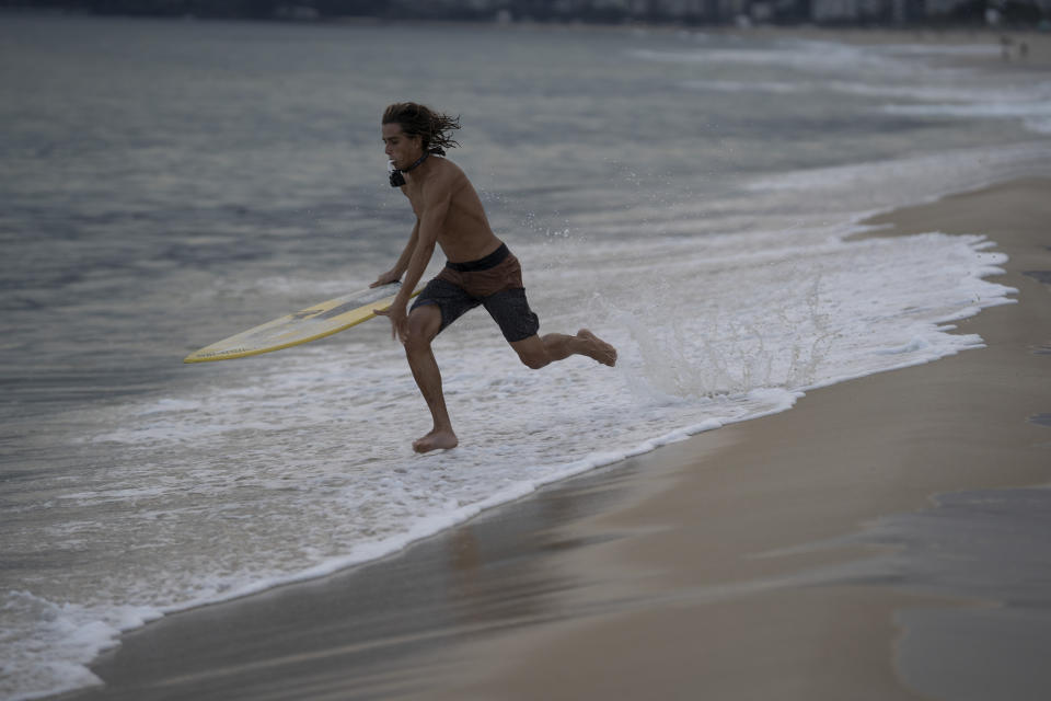 Leo Freitas runs to take a wave at Ipanema beach in Rio de Janeiro, Brazil, Monday, June 8, 2020. For the 18-year-old skimboard athlete, people need to take appropriate precautions when they go out, amid the new coronavirus pandemic, after the authorities have started to reopen gradually some businesses and easing some protective measures. (AP Photo/Leo Correa)