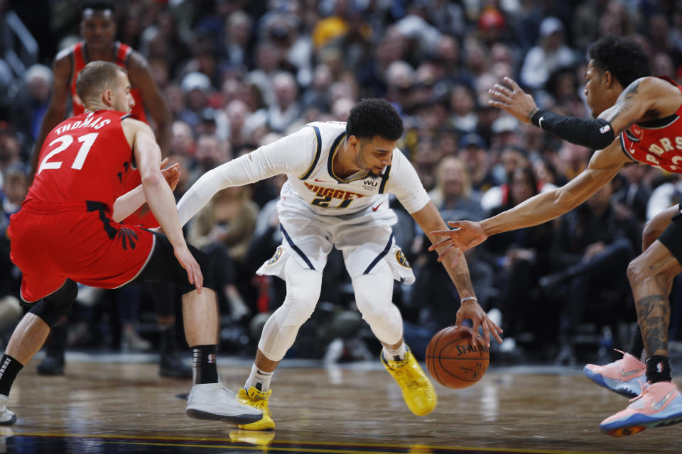 Denver Nuggets guard Jamal Murray, center, recovers the ball between Toronto Raptors guard Matt Thomas, left, and forward Patrick McCaw in the first half of an NBA basketball game Sunday, March 1, 2020. (AP Photo/David Zalubowski)