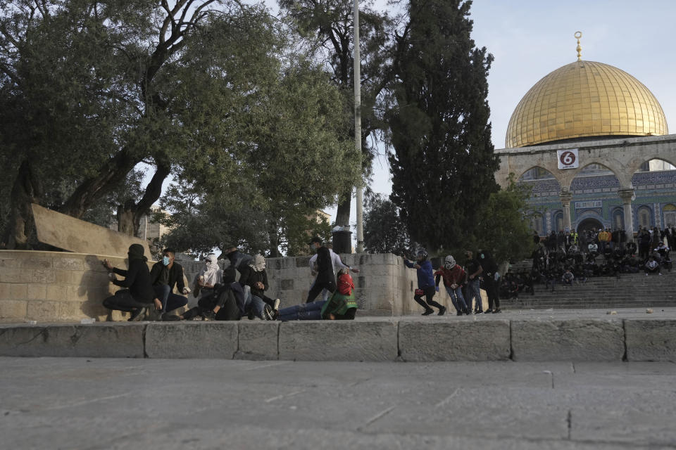 Palestinian protesters take cover as they clash with Israeli police at the Al Aqsa Mosque compound in Jerusalem's Old City, Friday, April 22, 2022. Israeli police and Palestinian youths clashed again at the major Jerusalem holy site sacred to Jews and Muslims on Friday despite a temporary halt to Jewish visits to the site, which are seen as a provocation by the Palestinians. (AP Photo/Mahmoud Illean)