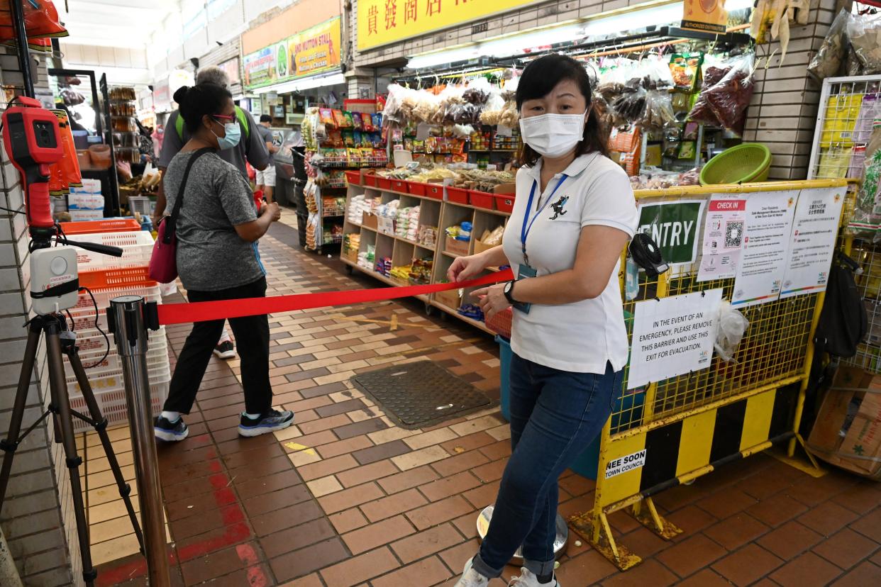 An officer stands at the entrance of a market to manage the flow of people in an attempt to curb the spread of the Covid-19 coronavirus in Singapore on October 9, 2021. / AFP / Roslan RAHMAN