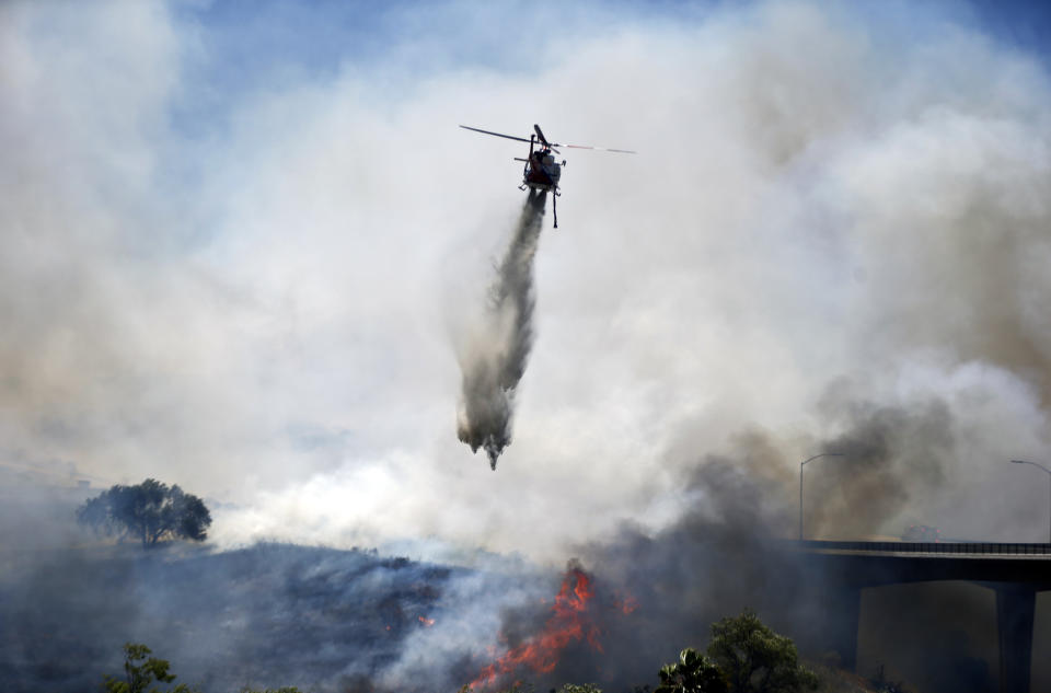 A helicopter attacks a wild fire burning Tuesday, May 13, 2014, in San Diego. Wildfires destroyed a home and forced the evacuation of several others Tuesday in California as a high-pressure system brought unseasonable heat and gusty winds to a parched state that should be in the middle of its rainy season. (AP Photo)