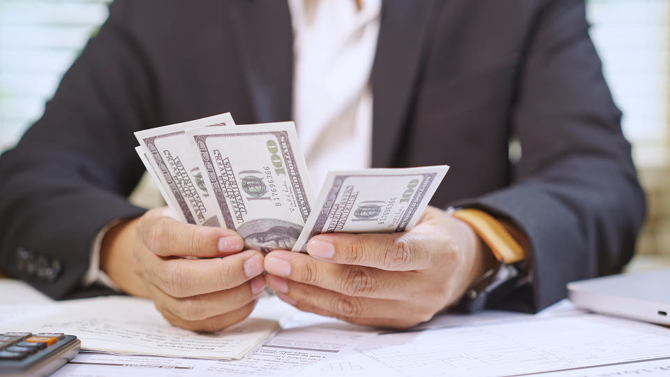 A businessman in a suit counting a stack of hundred-dollar bills, focusing on finance, wealth, and business success.