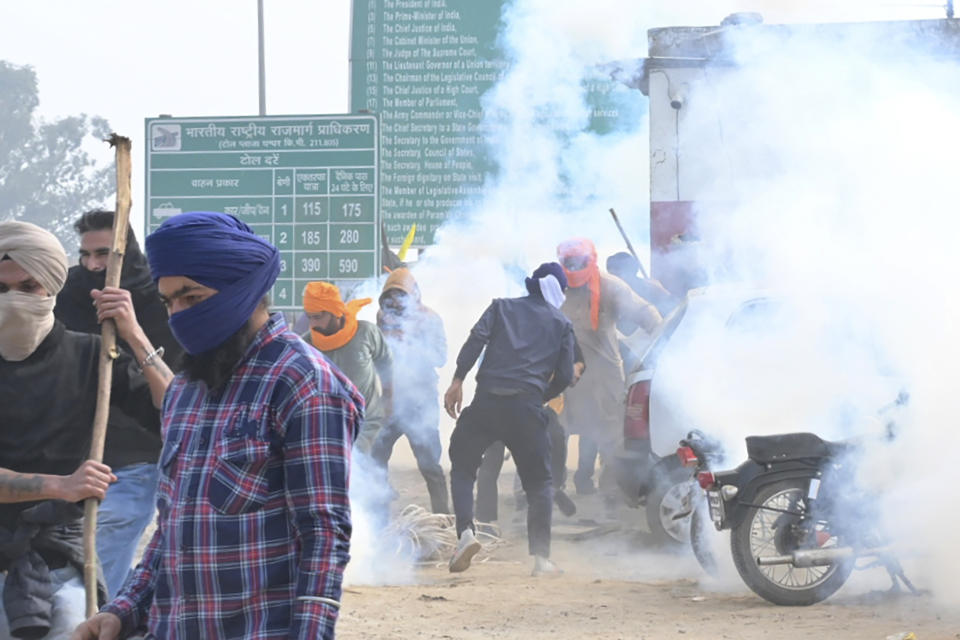 Farmers run for cover after police fired tear gas to disperse protesting farmers who were marching to New Delhi near the Punjab-Haryana border at Shambhu, India, Tuesday, Feb.13, 2024. Farmers are marching to the Indian capital asking for a guaranteed minimum support price for all farm produce. (AP Photo/Rajesh Sachar)