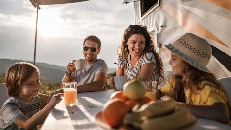 A smiling family of four having breakfast at sunrise while camping