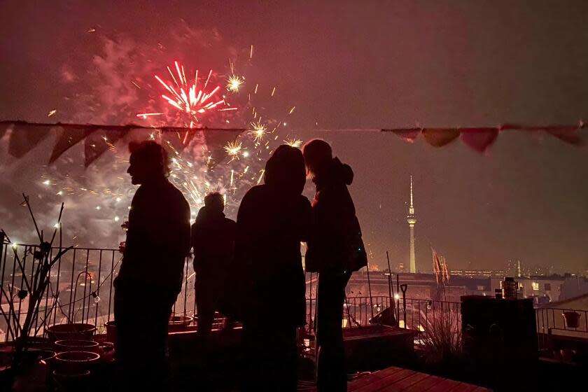 People celebrate the New Year on the roof of a building in Berlin, as fireworks explode in the air on January 1, 2024. (Photo by Barbara SAX / AFP) (Photo by BARBARA SAX/AFP via Getty Images)