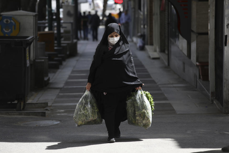 A woman wearing a face mask to protect against the new coronavirus carries her shopping in northern Tehran, Iran, Saturday, April 4, 2020. In the first working day after Iranian New Year holidays authorities have allowed some government offices and businesses to re-open with limited working hours, when schools, universities, and many businesses still are ordered to be closed aimed to prevent the spread of the virus. (AP Photo/Vahid Salemi)