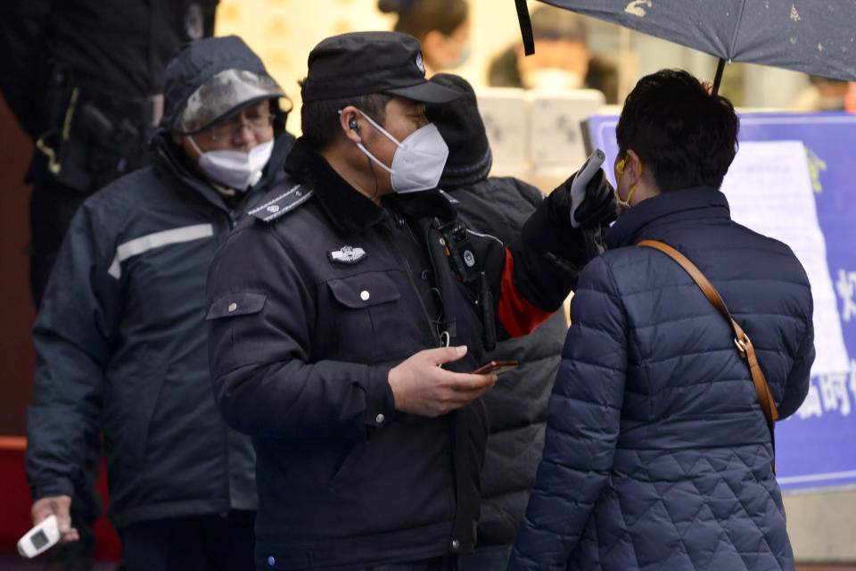 A policeman wearing a face mask takes a tourist's temperature at the Qinhuai scenic zone in Nanjing in eastern China's Jiangsu province, Saturday, Jan. 25, 2020. The virus-hit Chinese city of Wuhan, already on lockdown, banned most vehicle use downtown and Hong Kong said it would close schools for two weeks as authorities scrambled Saturday to stop the spread of an illness that is known to have infected more than 1,200 people and killed 41, according to officials. (Chinatopix via AP)