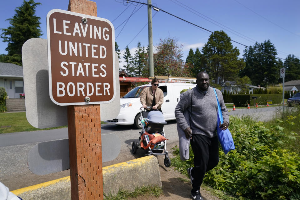 Canadian residents Philip Owira, right, and Katherine Nichol walk with their baby across a small ditch from Canada into Peace Arch Historical State Park to visit a friend there, Tuesday, June 8, 2021, in Blaine, Wash. The border has been closed to nonessential travel since March 2020, but Canadians have been allowed to walk over the ditch into the U.S. park. (AP Photo/Elaine Thompson)