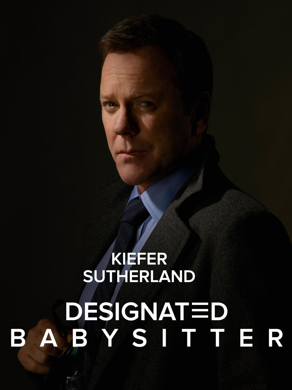 Kiefer in a tailored suit and tie holding glasses, posing with a serious expression, with caption "Kiefer Sutherland Designated Babysitter"