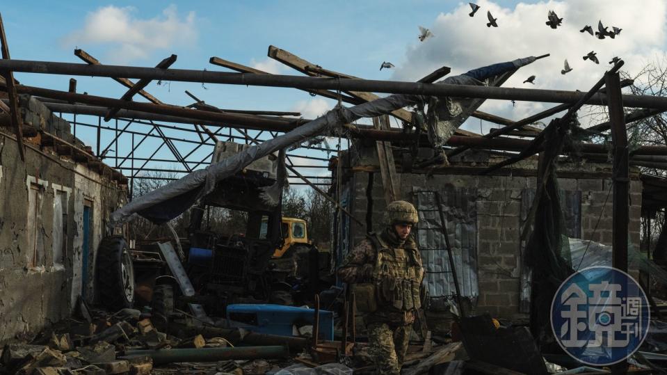 一名士兵在爆炸後的廢墟中行走，觀察一棟受損的房屋。房屋飽受衝突摧殘，只剩幾堵牆還矗立著。