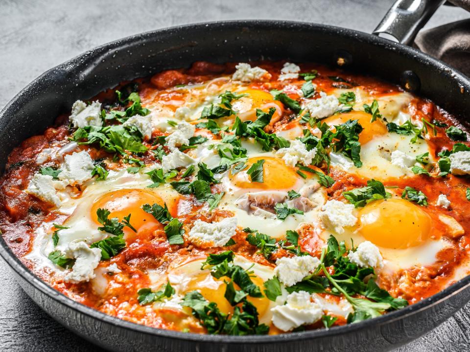 Homemade shakshuka, fried eggs, onion, bell pepper, tomatoes and parsley in a pan. Gray background. Top view